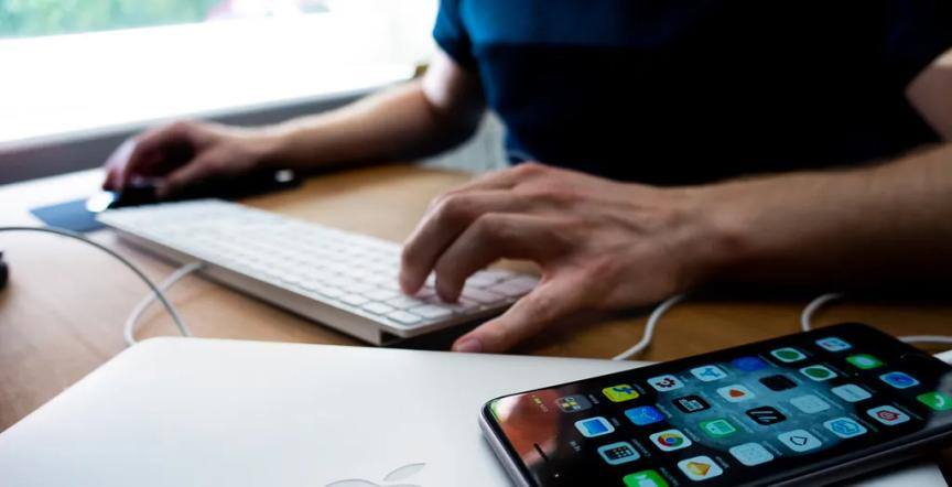 An iOS developer typing something on a keyboard with an iPhone by his side